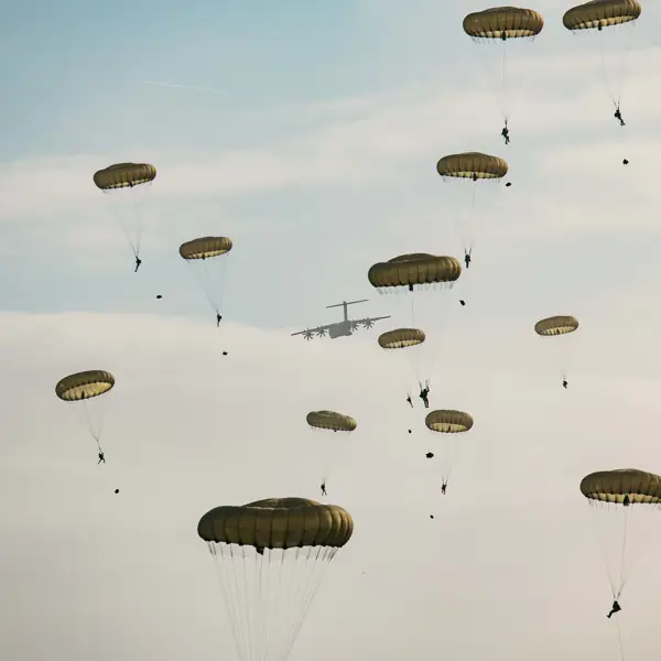 Multiple parachutes with individuals descending from a military aircraft in the sky.