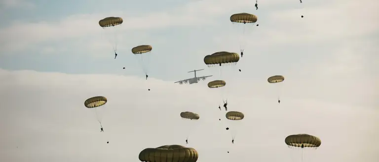 Multiple parachutes with individuals descending from a military aircraft in the sky.