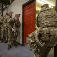 A line of soldiers in uniform prepare to enter a room with their weapons.