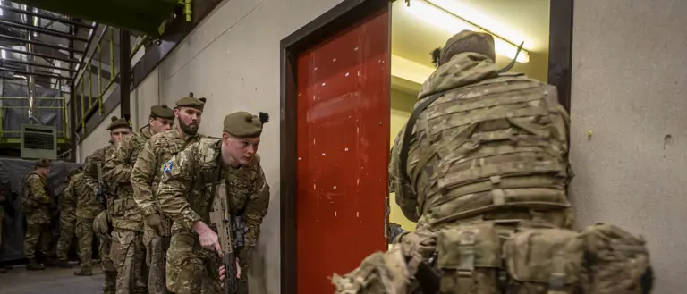 A line of soldiers in uniform prepare to enter a room with their weapons.