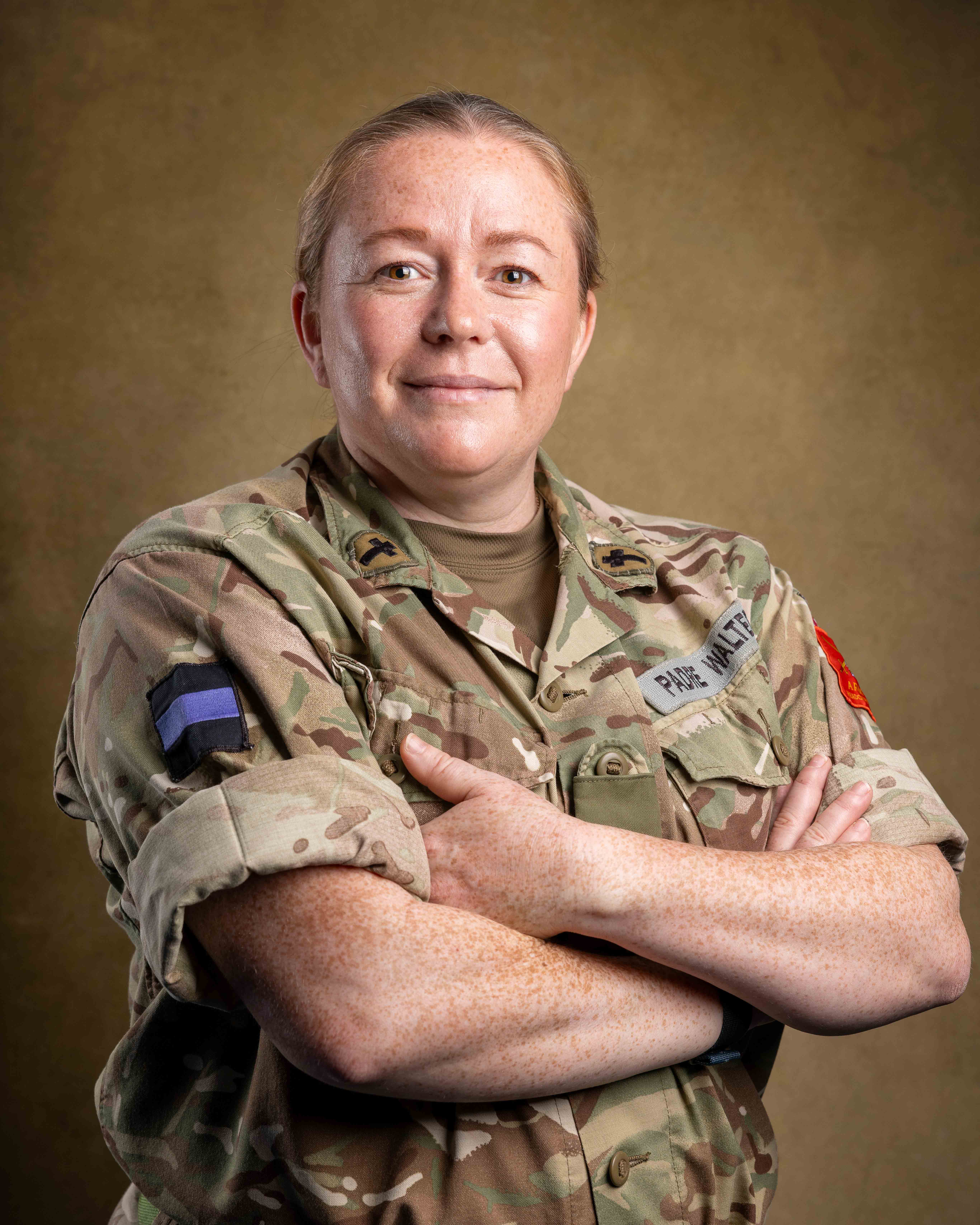 Reverend Amy Walters stood with her arms folded posing for a portrait with a studio backdrop wearing her uniform.