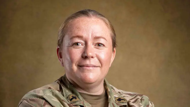 Reverend Amy Walters stood with her arms folded posing for a portrait with a studio backdrop wearing her uniform.