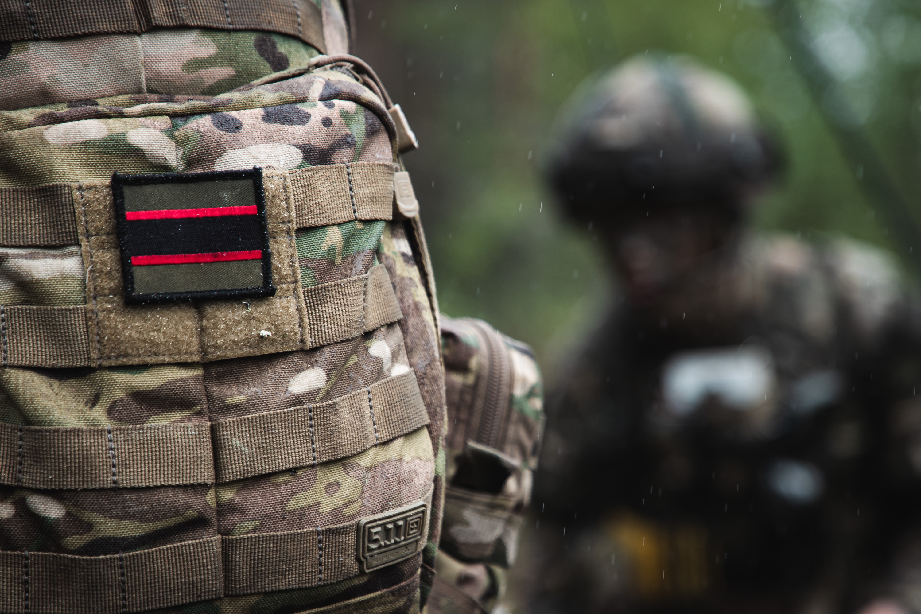 The rifles flash shown on a camouflage colour back pack bag. The flash is olive green, red and black horizontal stripes in a rectangle shape. 
