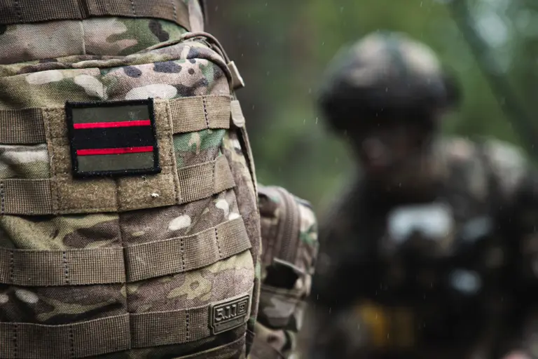 The rifles flash shown on a camouflage colour back pack bag. The flash is olive green, red and black horizontal stripes in a rectangle shape. 