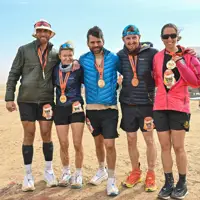 Five people stood in running gear and coats with medals hanging from their necks in a desert background.