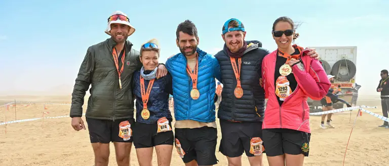 Five people stood in running gear and coats with medals hanging from their necks in a desert background.