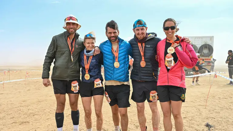 Five people stood in running gear and coats with medals hanging from their necks in a desert background.