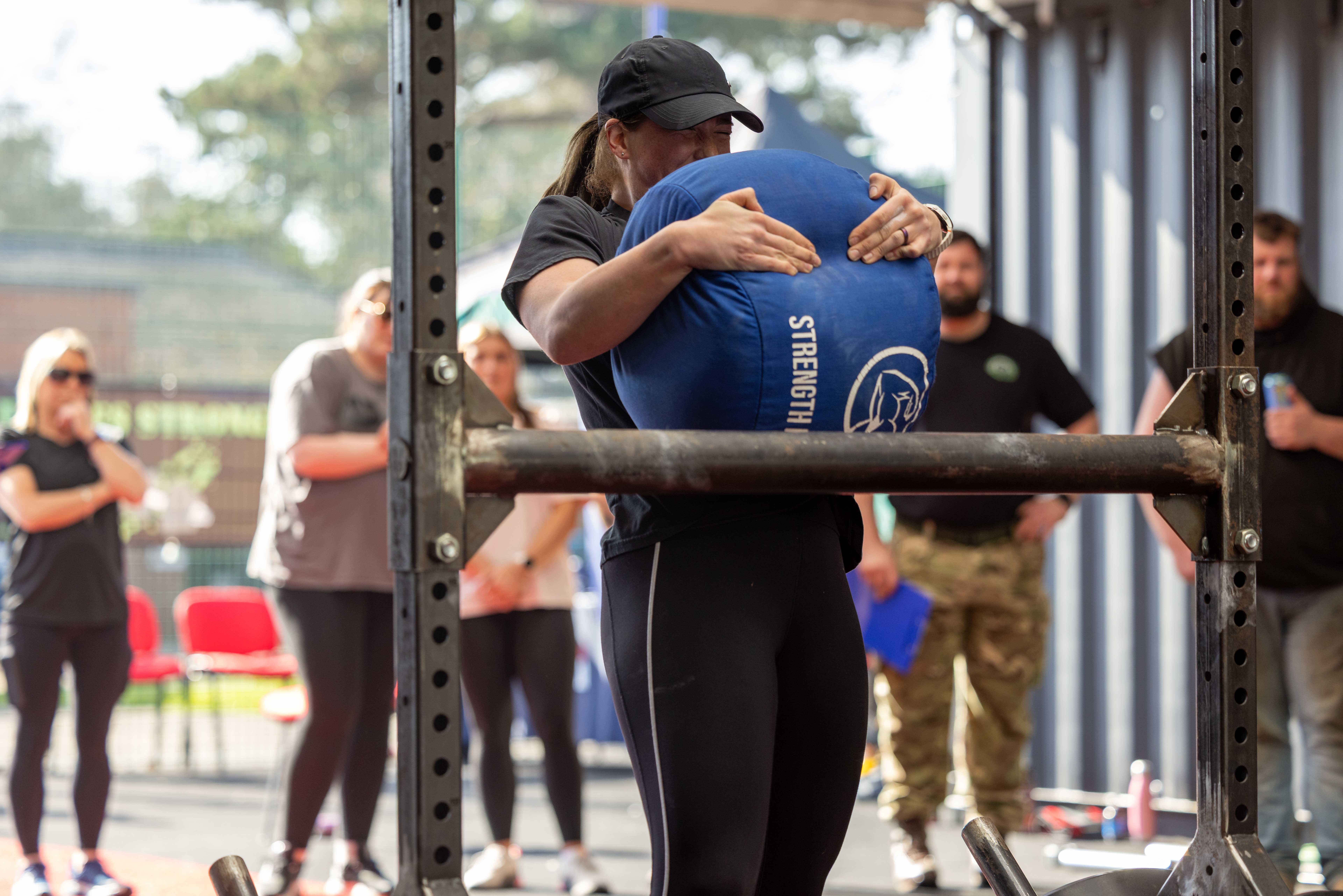 A person in athletic wear lifts a large blue sandbag marked 