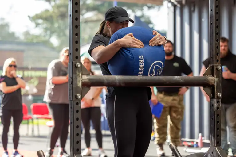 A person in athletic wear lifts a large blue sandbag marked