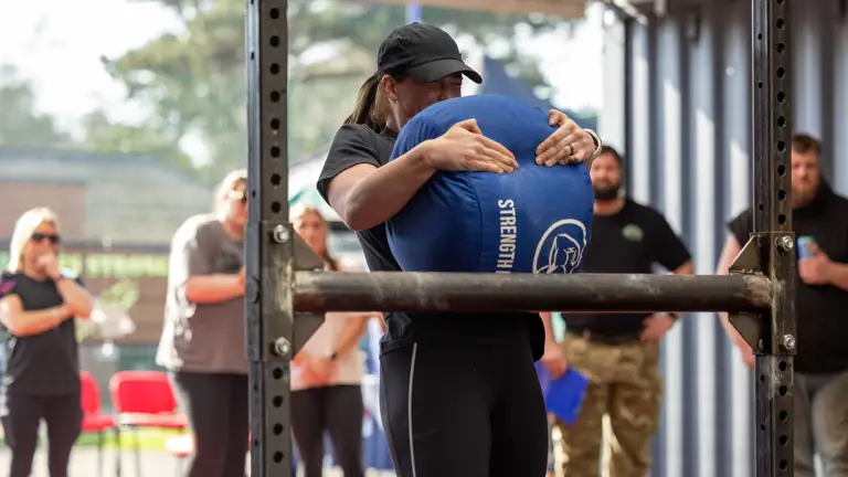 A person in athletic wear lifts a large blue sandbag marked