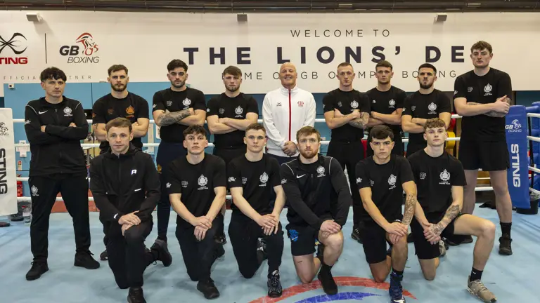 A group of men in black tshirts and shorts pose for a group photo with a man in a white shirt and shorts.