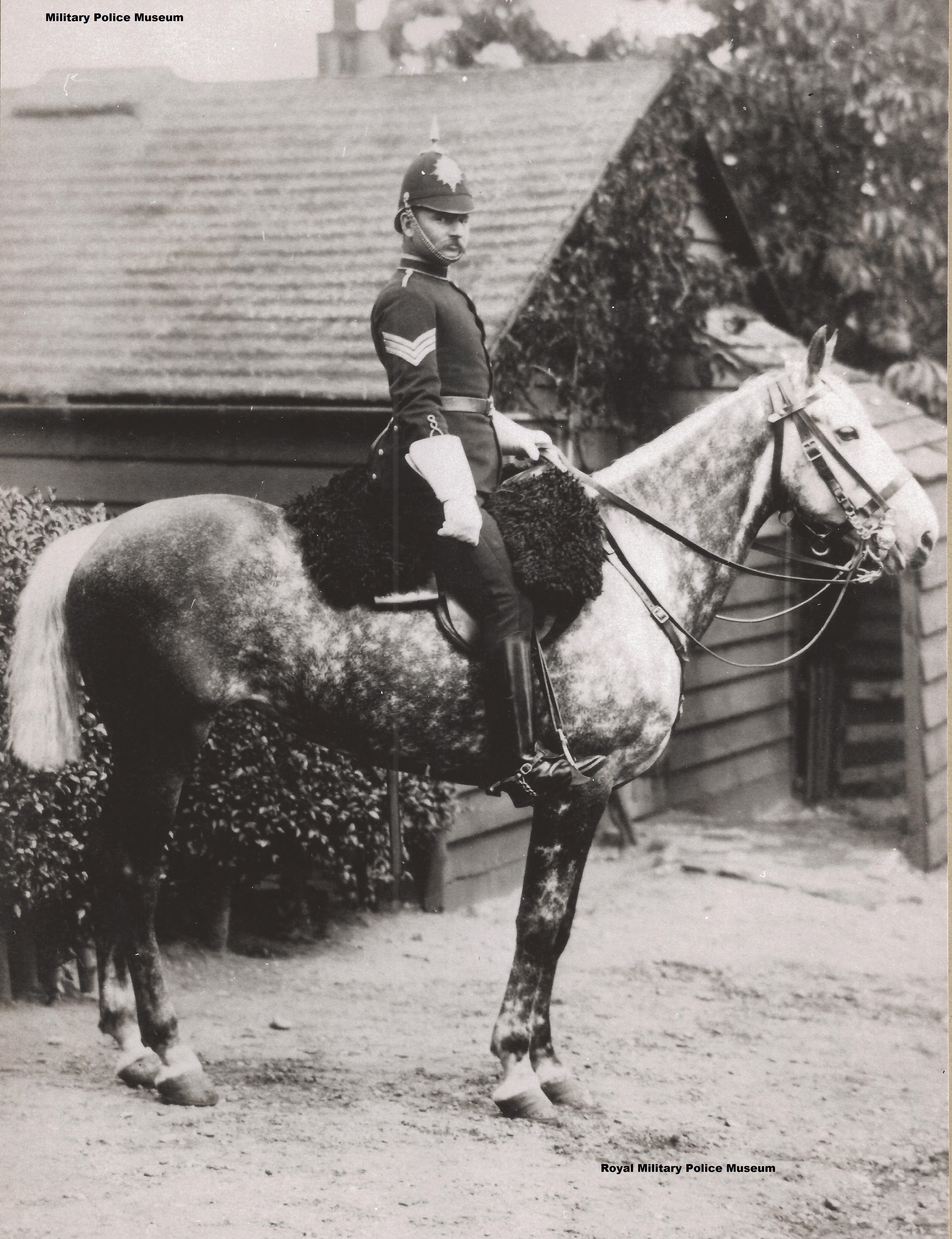 A mounted police officer in formal uniform sits confidently on a dappled horse. The background shows rustic wooden buildings and foliage, evoking a historical atmosphere.