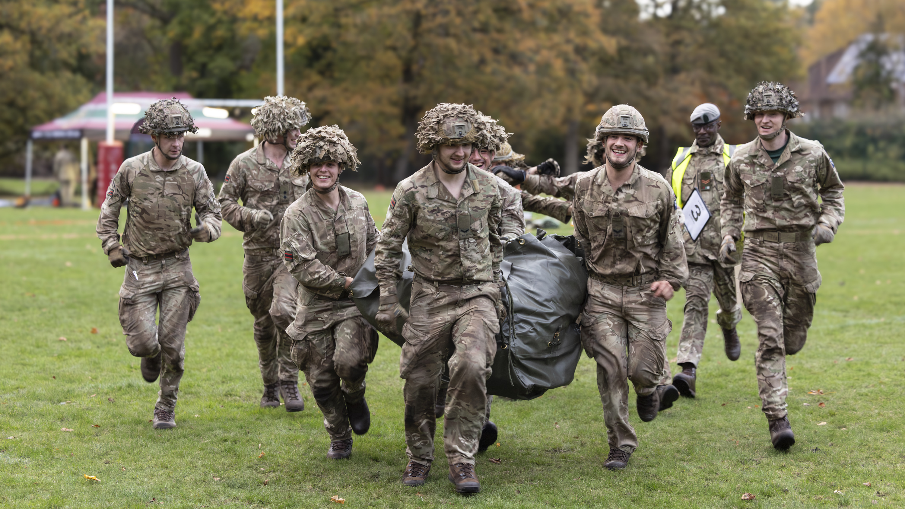 Group of soldiers in camouflage uniforms running together on a grassy field during a training exercise.