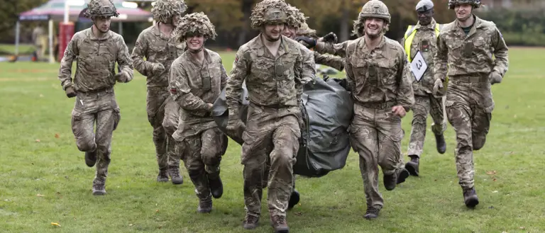 Group of soldiers in camouflage uniforms running together on a grassy field during a training exercise.