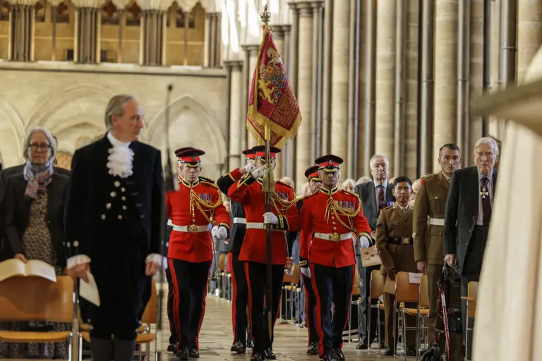 Men in red ceremonial uniforms carry a red and gold ceremonial flag through a cathedral.