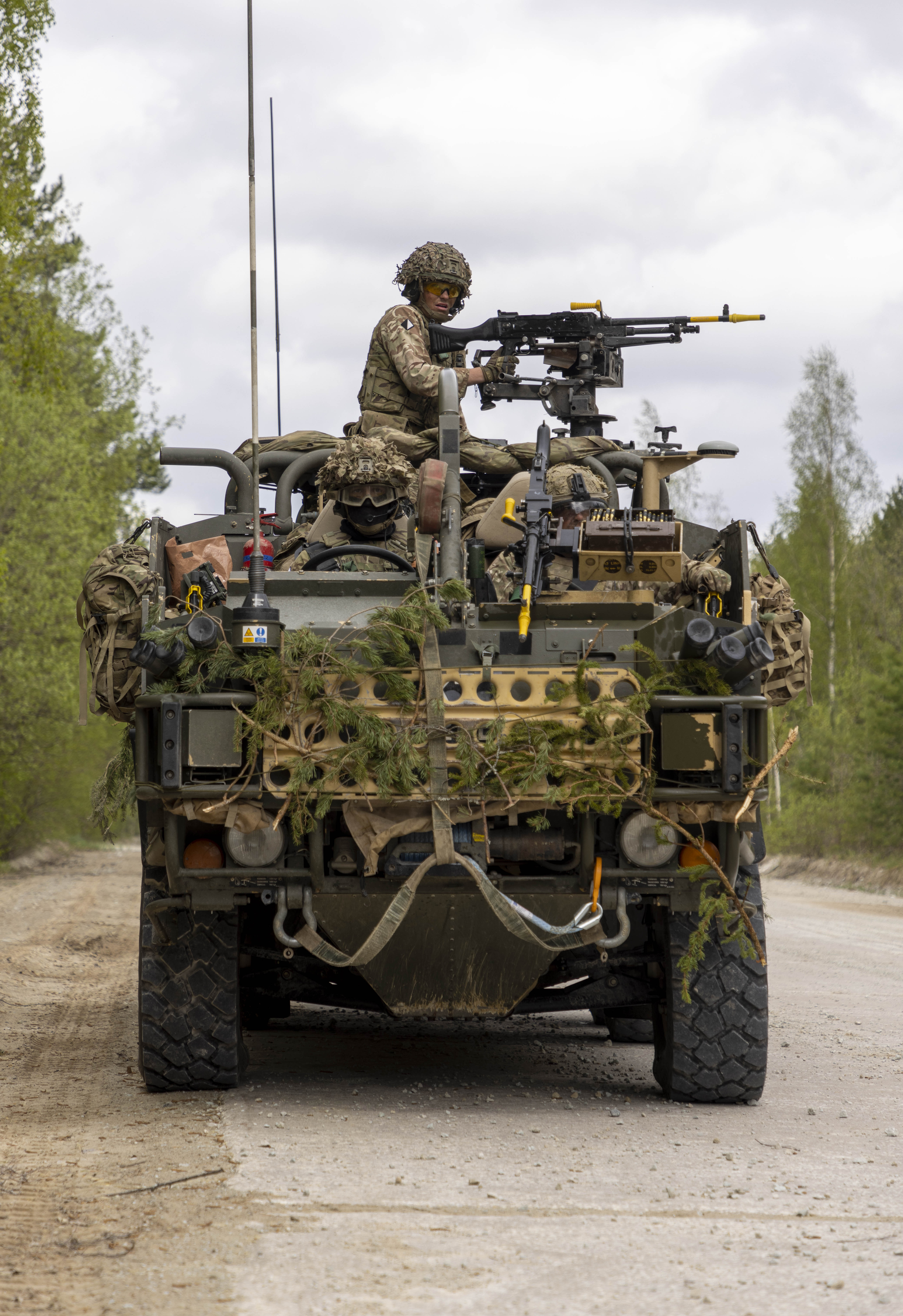 A Jackal vehicle is being manned with the weapon operated by a soldier. The vehicle is seen driving down a road in a wooded area on exercise. 