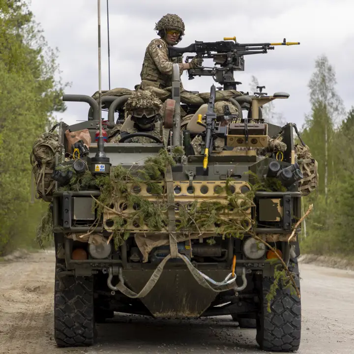 A Jackal vehicle is being manned with the weapon operated by a soldier. The vehicle is seen driving down a road in a wooded area on exercise.