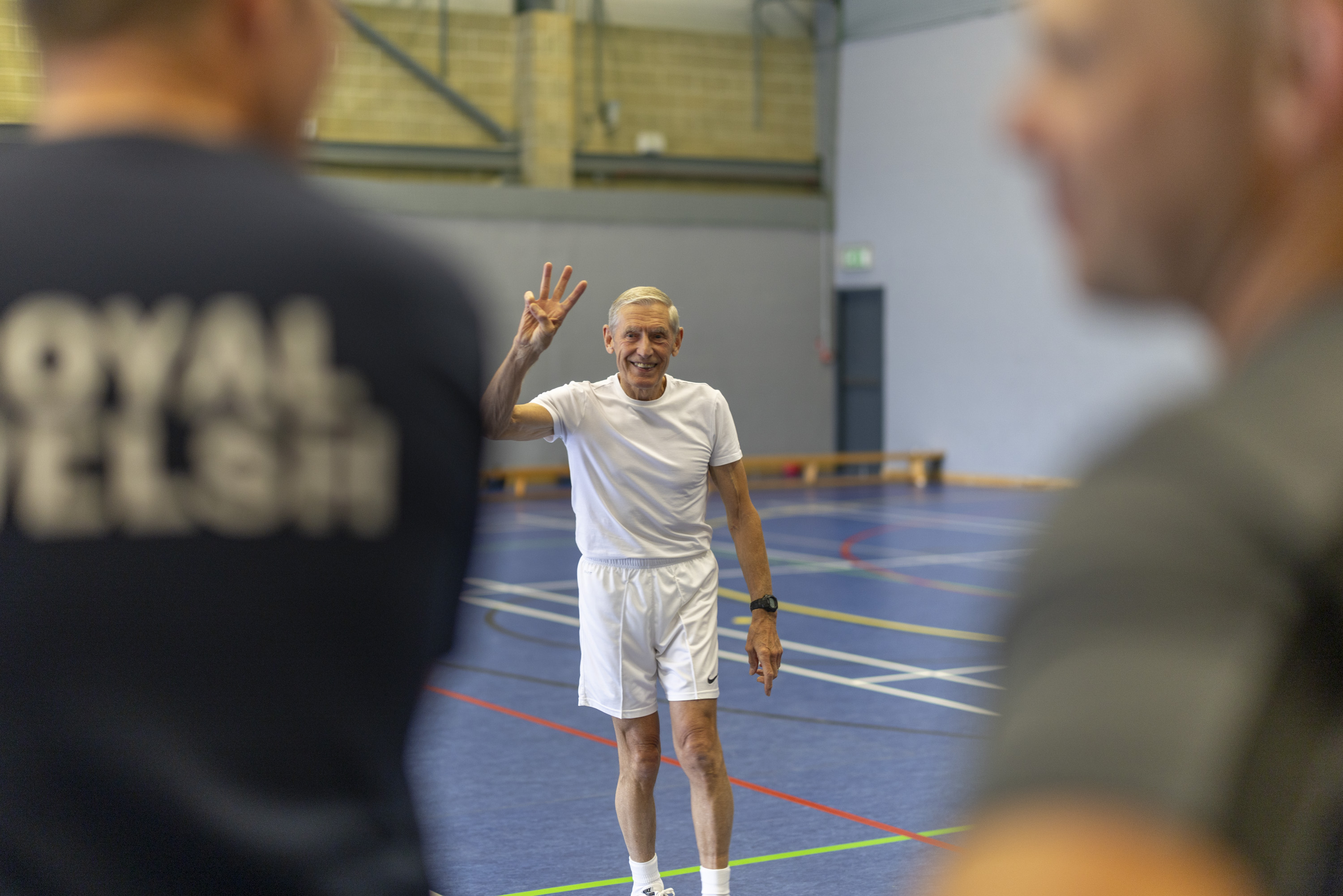A man in a white shirt holds up three fingers during a fitness class.