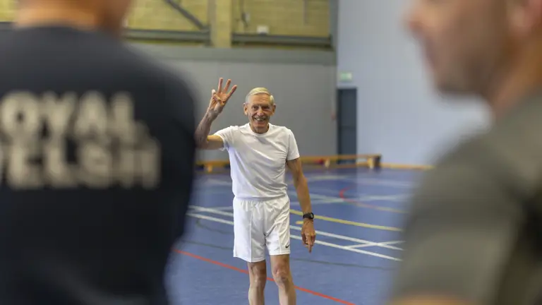 A man in a white shirt holds up three fingers during a fitness class.