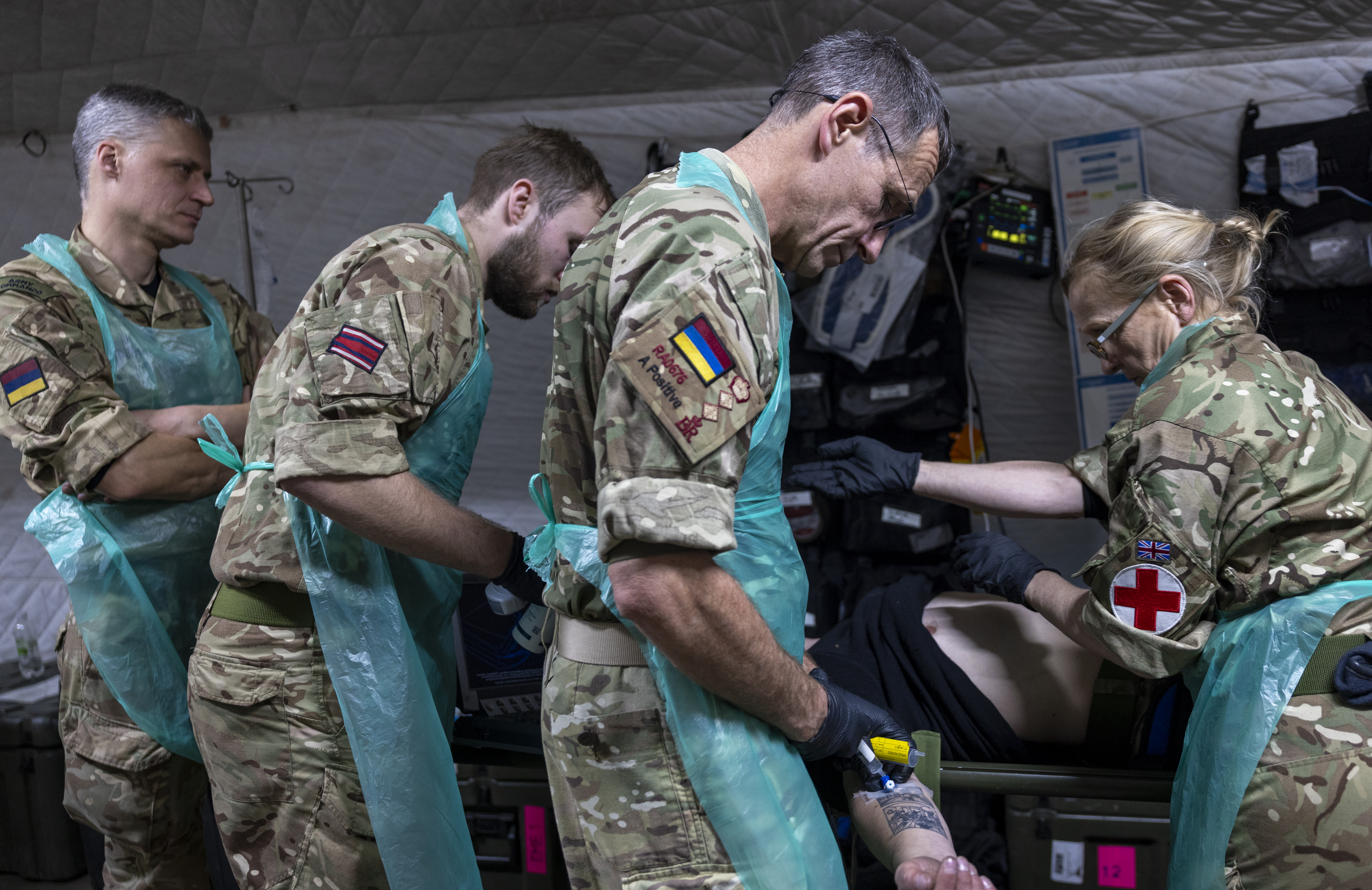 A group of military personnel in camouflage uniforms and protective aprons are attending to a person.