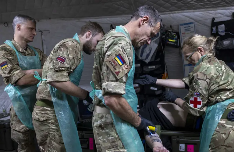 A group of military personnel in camouflage uniforms and protective aprons are attending to a person.