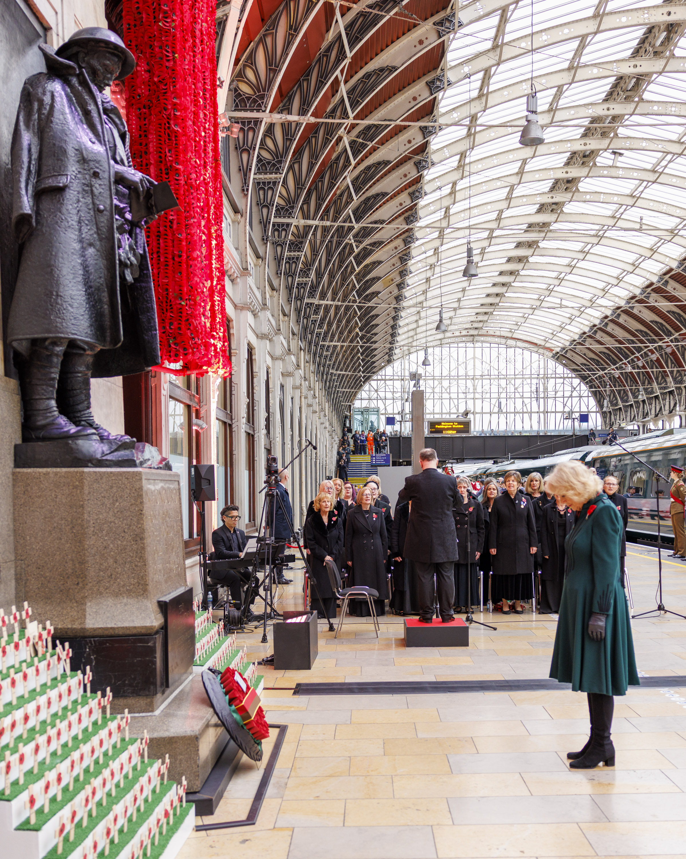 Her Majesty the Queen bows her head at a war memorial. She is wearing a green dress. 