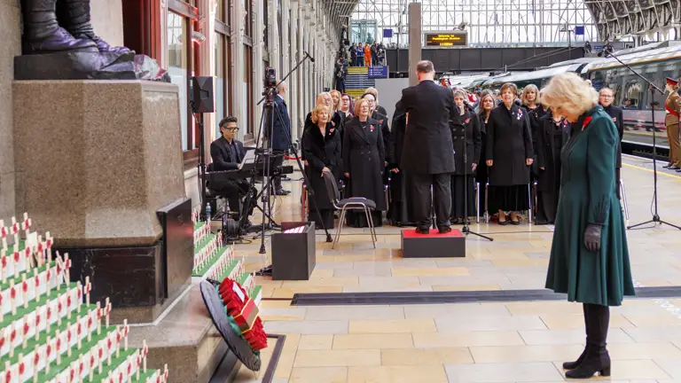 Her Majesty the Queen bows her head at a war memorial. She is wearing a green dress.