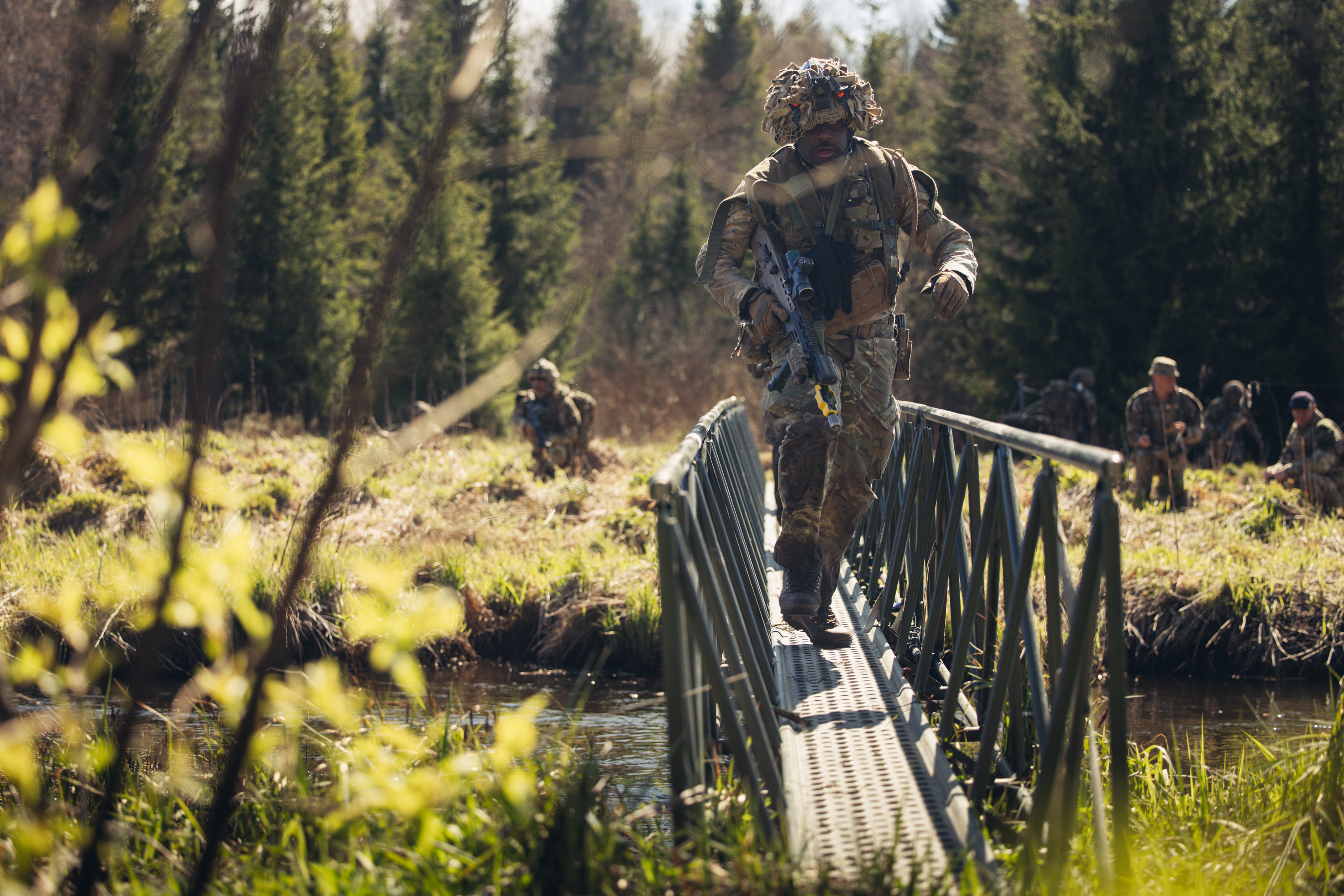 A soldier in uniform crosses a bridge above a river.