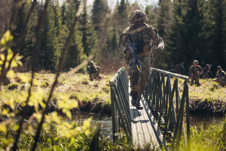A soldier in uniform crosses a bridge above a river.