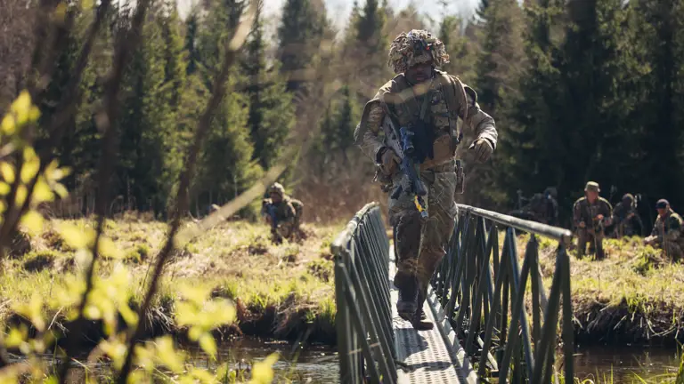 A soldier in uniform crosses a bridge above a river.