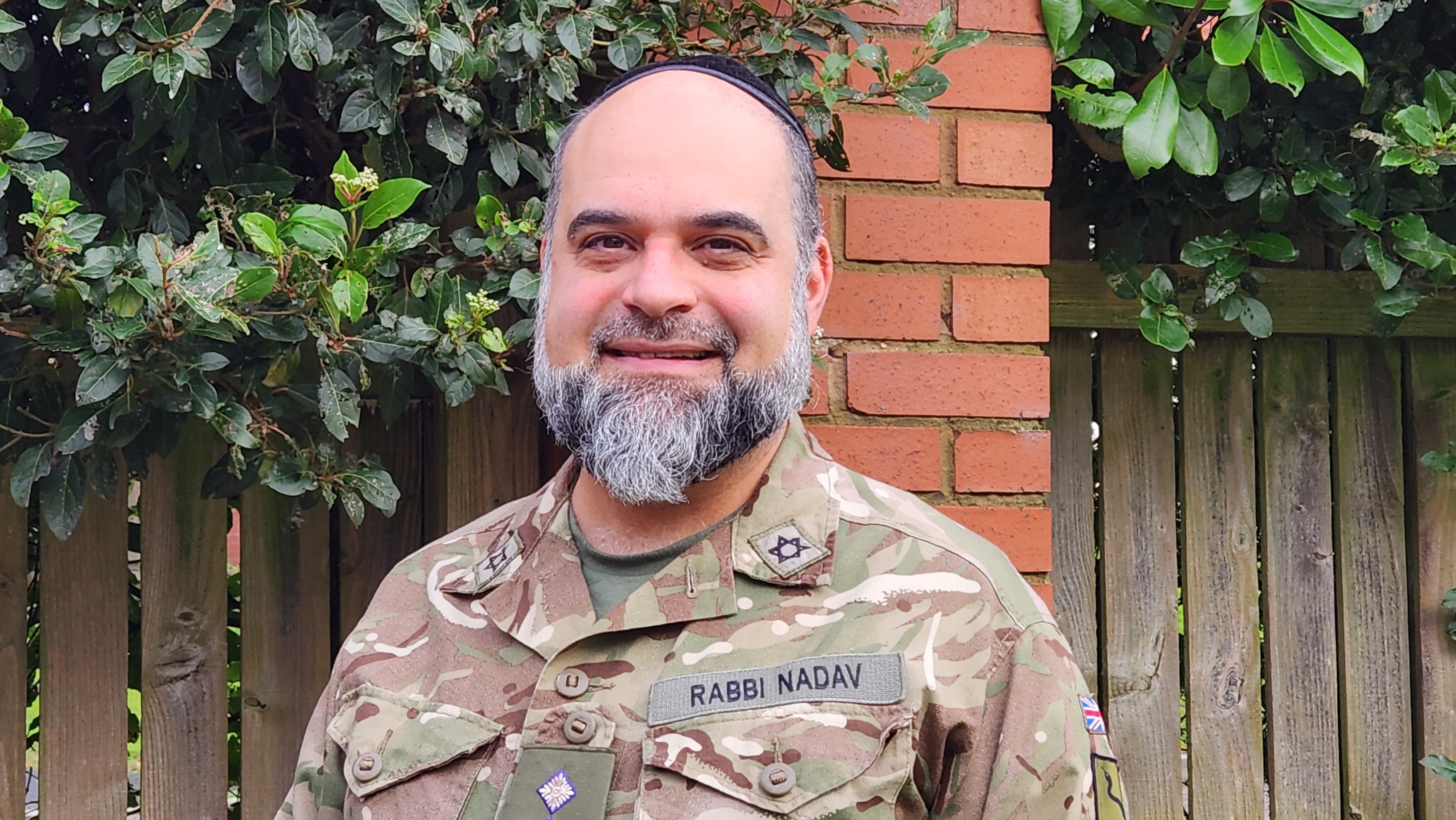 Rabbi Nir Nadav shown smiling for a portrait wearing his uniform and jewish headdress. 