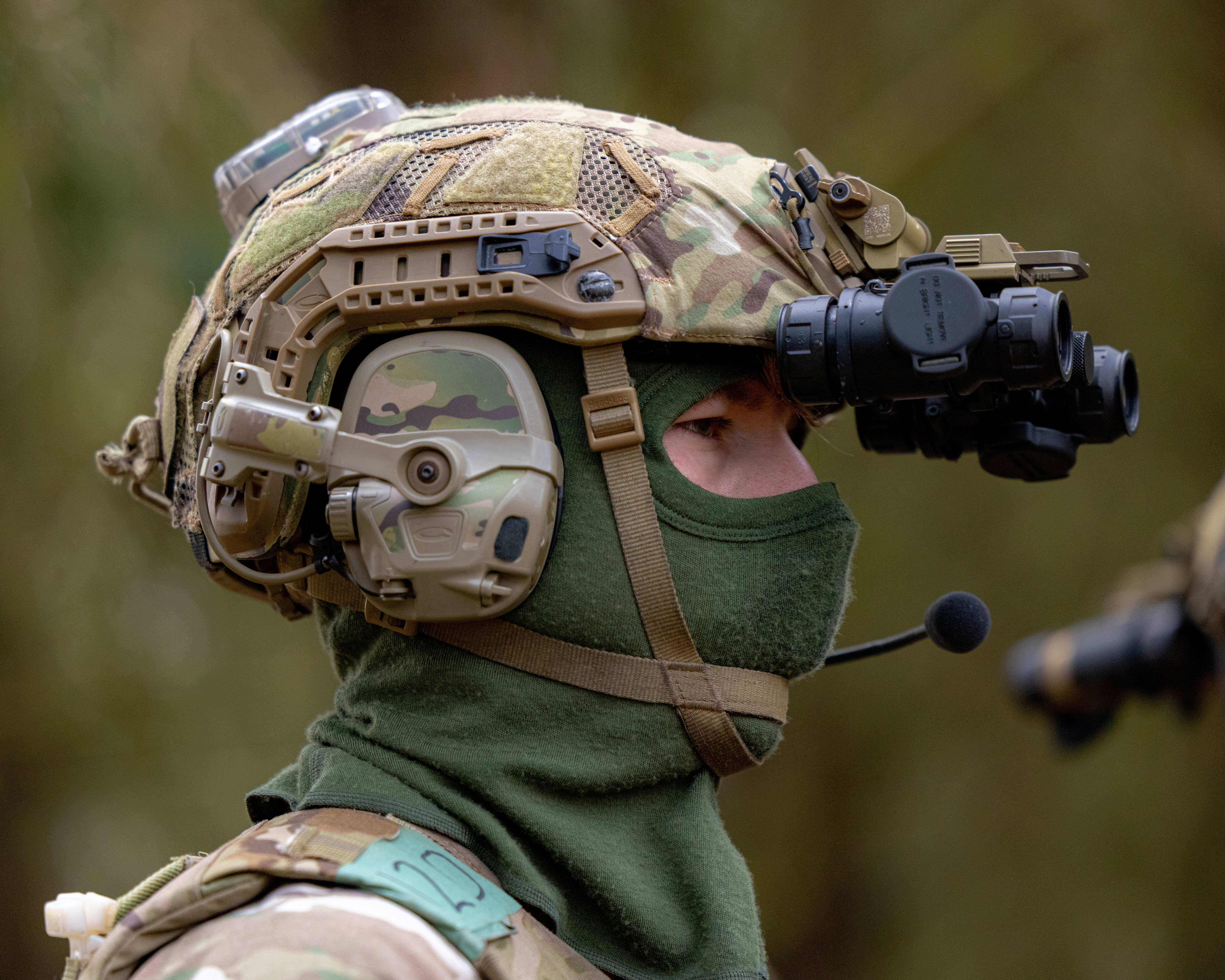 An individual in military camouflage gear is wearing a tactical helmet equipped with a night vision device.