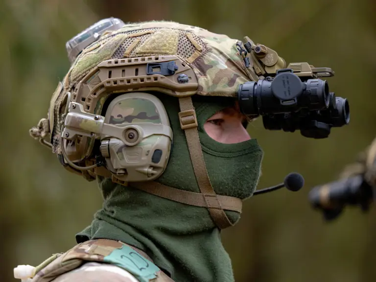 An individual in military camouflage gear is wearing a tactical helmet equipped with a night vision device.