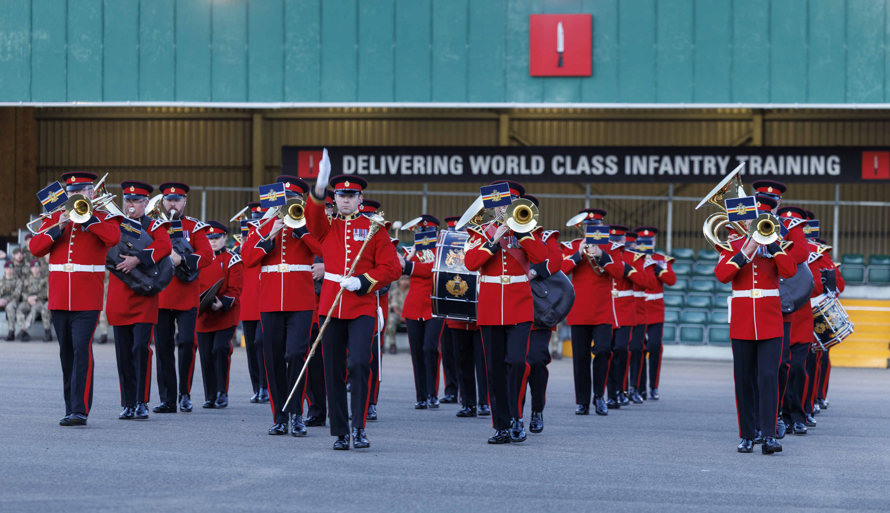 An Army band in red and black ceremonial uniform playing instruments. 