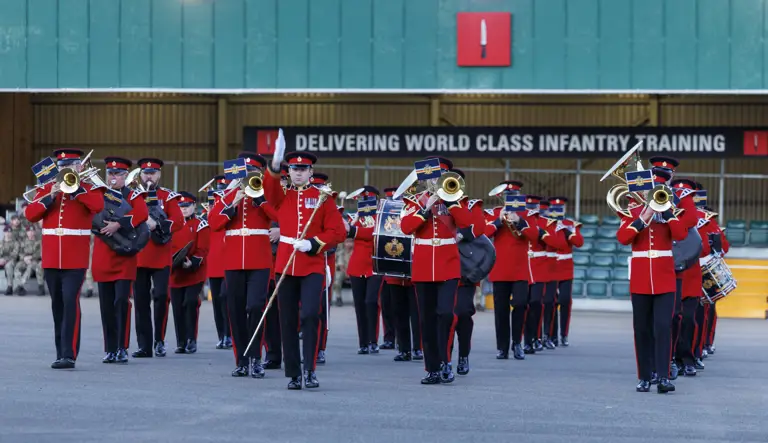 An Army band in red and black ceremonial uniform playing instruments. 