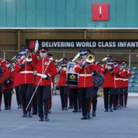 An Army band in red and black ceremonial uniform playing instruments.