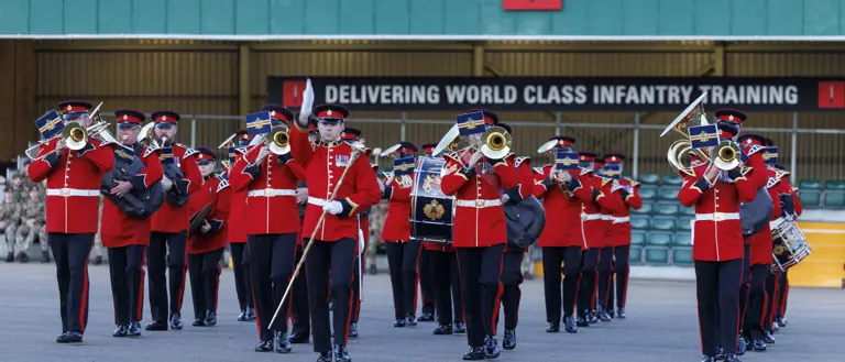 An Army band in red and black ceremonial uniform playing instruments.