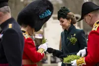Her Royal Highness The Princess of Wales smiles as she hands a shamrock to a man in a red tunic with a bearskin hat.