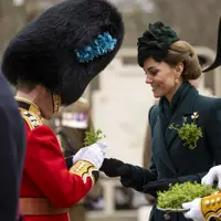 Her Royal Highness The Princess of Wales smiles as she hands a shamrock to a man in a red tunic with a bearskin hat.