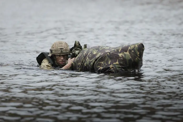 Soldier in camouflage swimming through water, holding a waterproof bag. 
