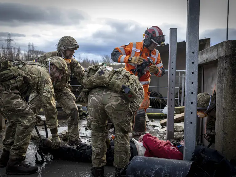 Soldiers in camouflage uniforms assist injured individuals.