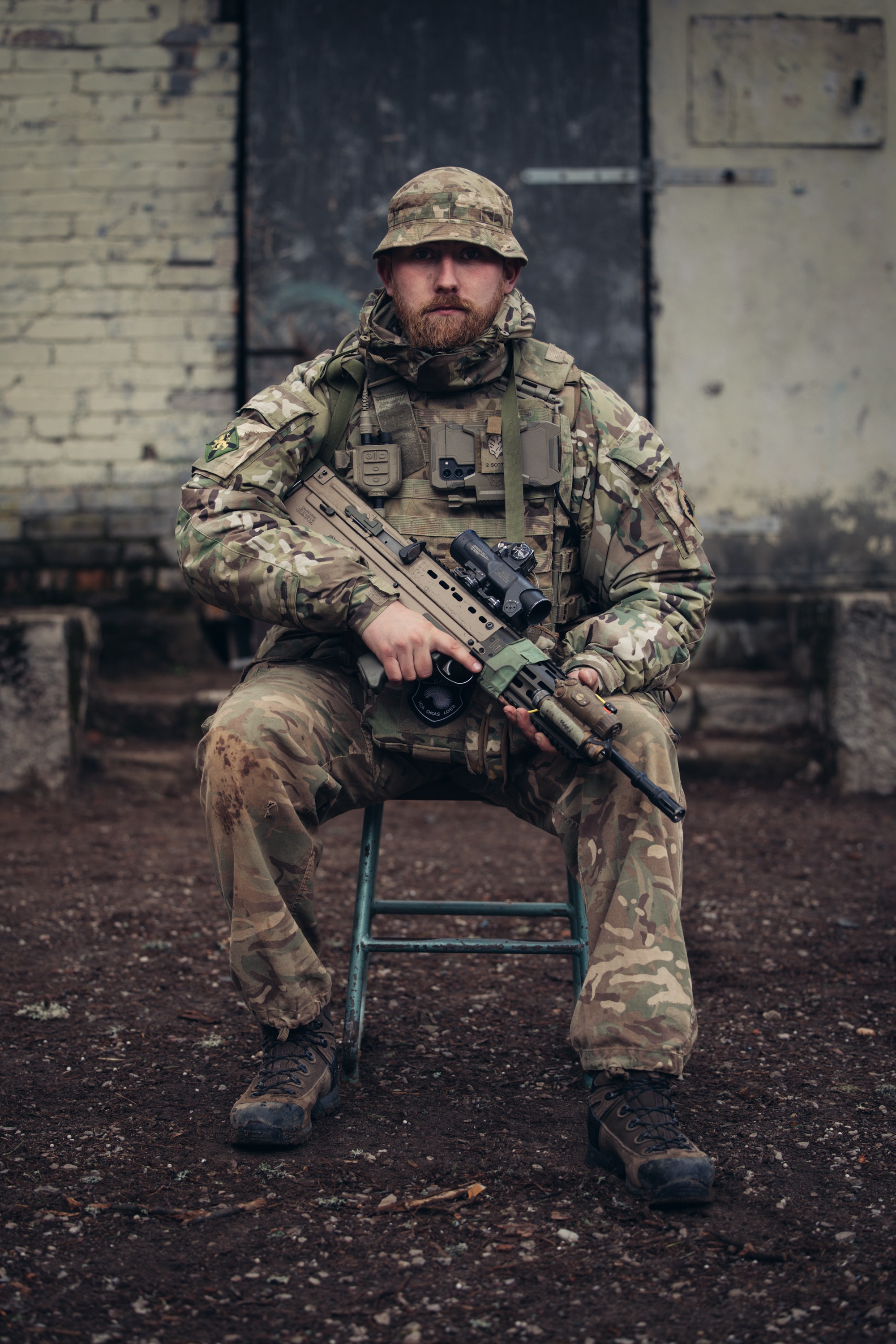 A soldier in uniform is seated with his weapon. 