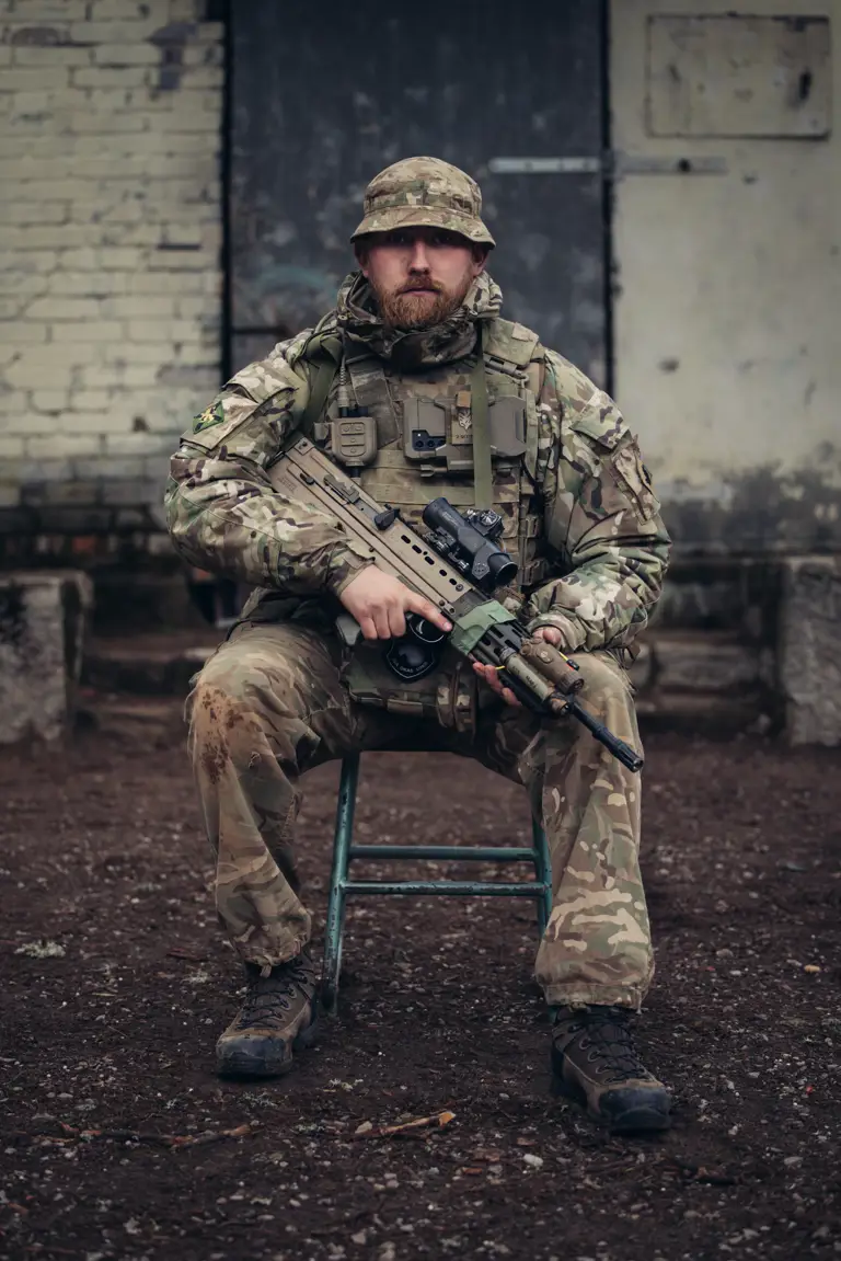 A soldier in uniform is seated with his weapon.