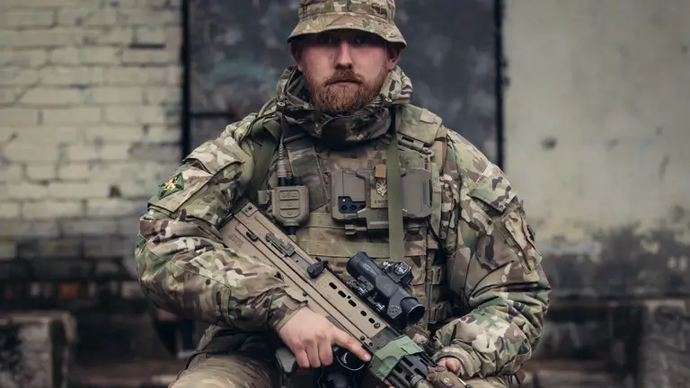 A soldier in uniform is seated with his weapon.