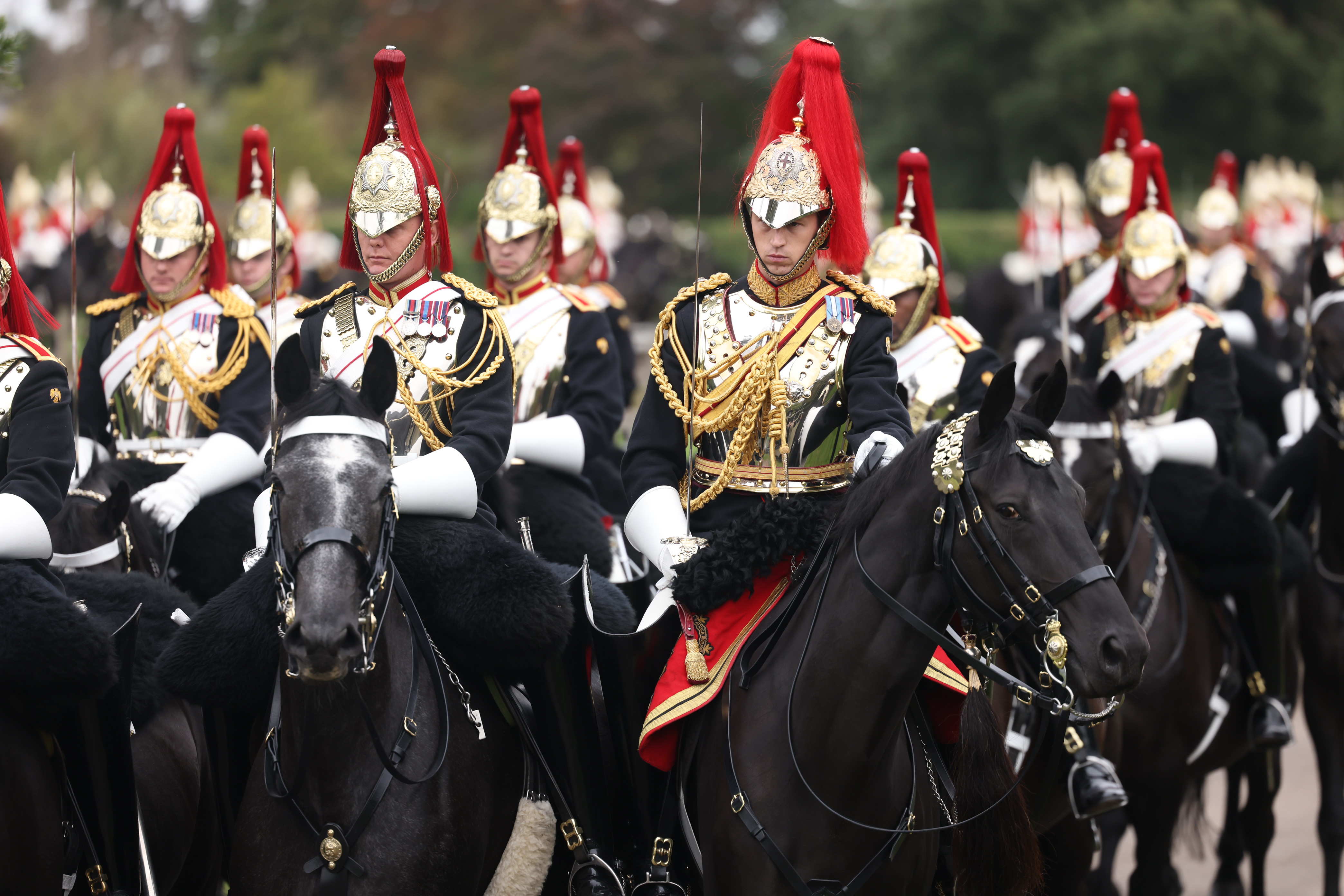 Soldiers in black ceremonial uniform sit on horseback while holding swords. 