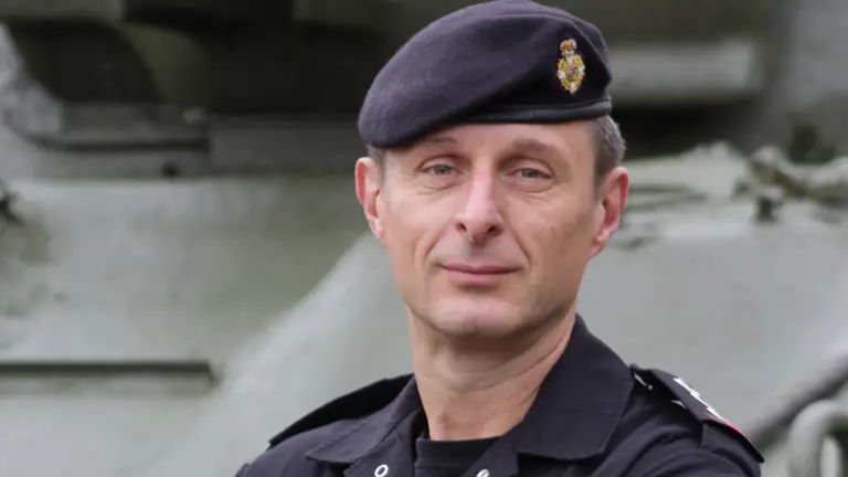 Reverend Mark Nightingale, wearing his black RTR coveralls and beret is stood posing arms folded in front of a tank.