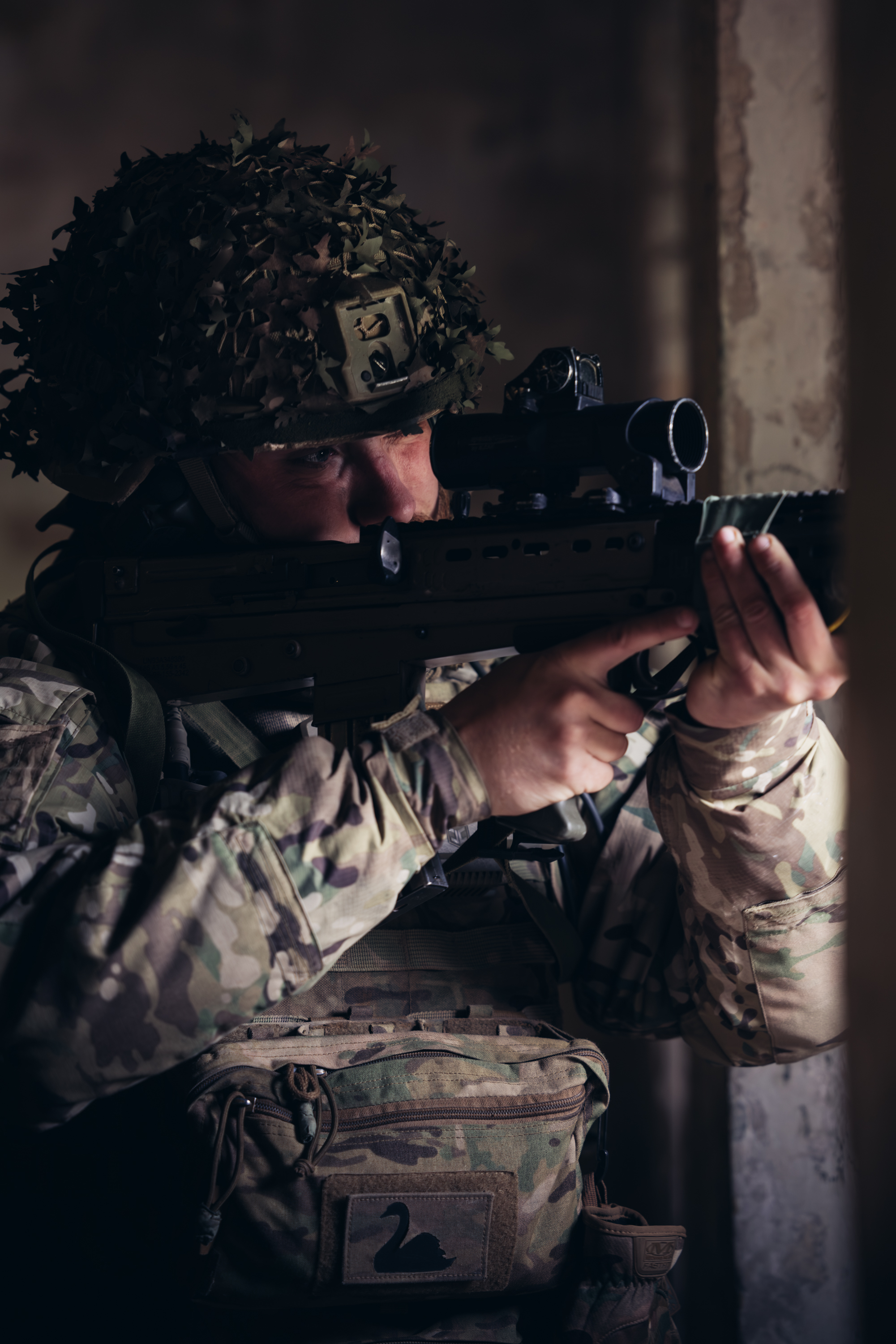 A soldier in uniform looks down the scope of his rifle. 