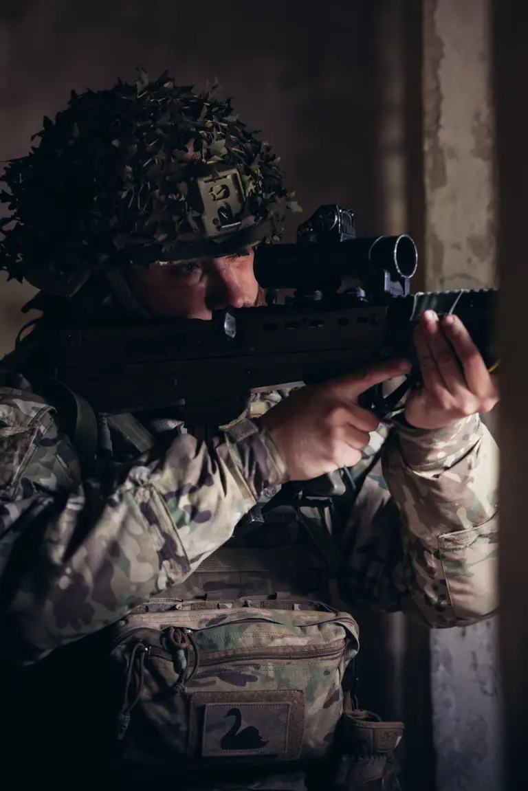 A soldier in uniform looks down the scope of his rifle.