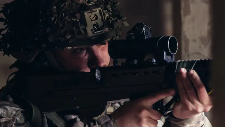 A soldier in uniform looks down the scope of his rifle.