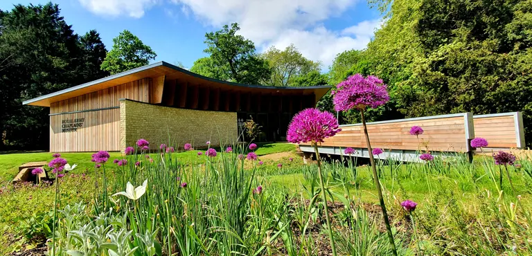 A museum is pictured from the exterior, purple flowers are present in the foreground.